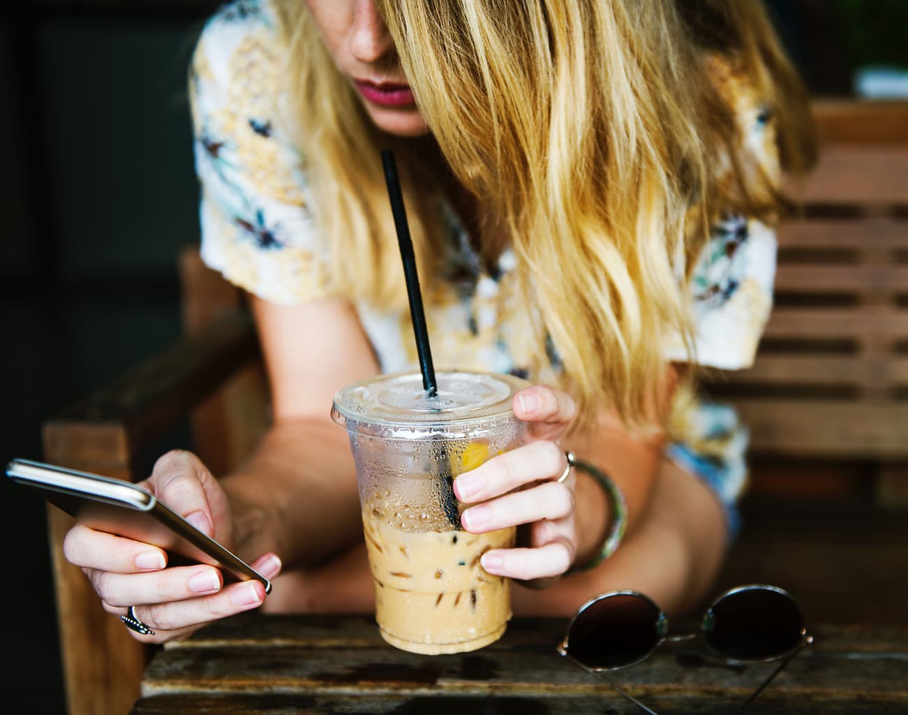 Chica usando las redes sociales en su teléfono mientras sostiene un café